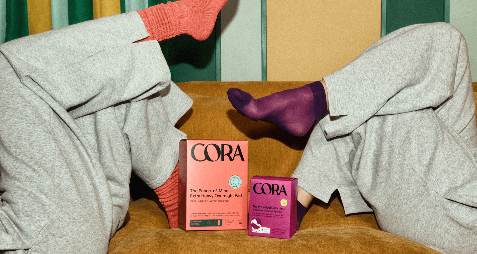 Cora Peace-of-Mind Extra Heavy Overnight Pads and Invisi-feel Daily Liners on a sofa, with cozy loungewear feet in frame
